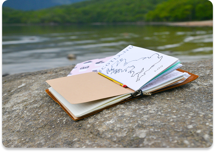 Open notebook on rock by a lake.